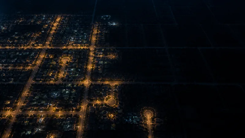 Aerial view of suburban neighborhood grid at night with some blocks lit in warm amber and others fading into darkness