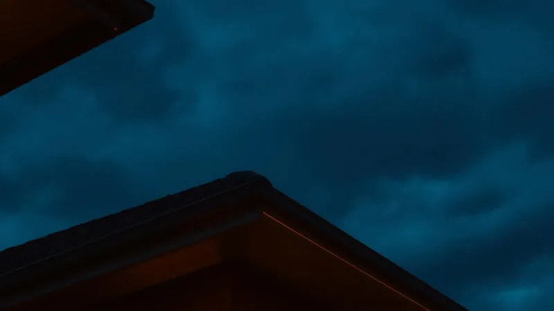Dusk rooftop silhouette with warm amber eave light evoking a roofing company after-hours reputation